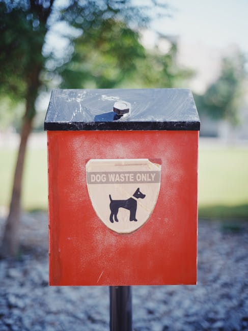 A black trash or rubbish bin with an orange label reading 'Garage Deca' and the number '36' in orange, positioned on a paved area outdoors. The bin's lid is blue with a handle, and there are small sti