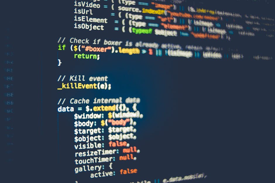 A close-up view of a laptop screen displaying lines of programming code within a code editor, situated on a desk or table. The screen shows a mixture of text in various colors indicating syntax highli