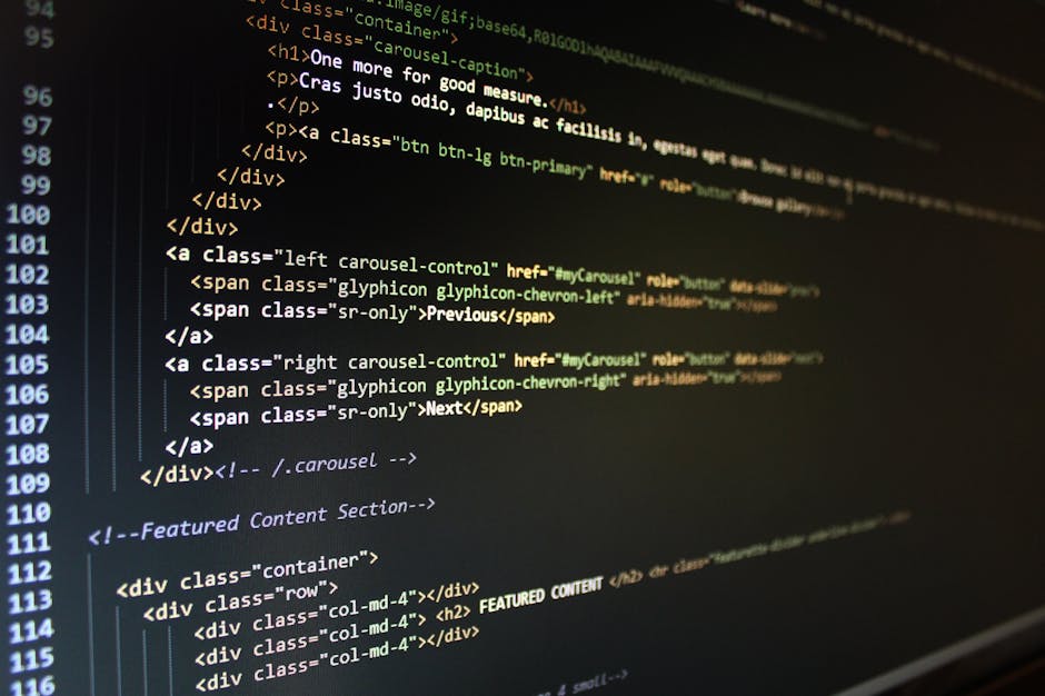 Close-up of a person's hands typing on a sleek, silver laptop with a dark screen displaying lines of colorful coding and programming scripts. The laptop is set on a smooth, dark table in a dimly lit e